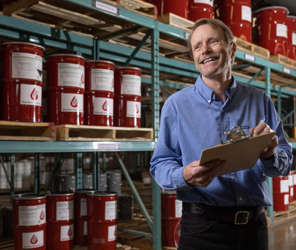 Man organizing inventory in warehouse with red barrels.