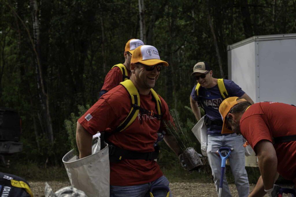 Group planting trees in forest with tools.