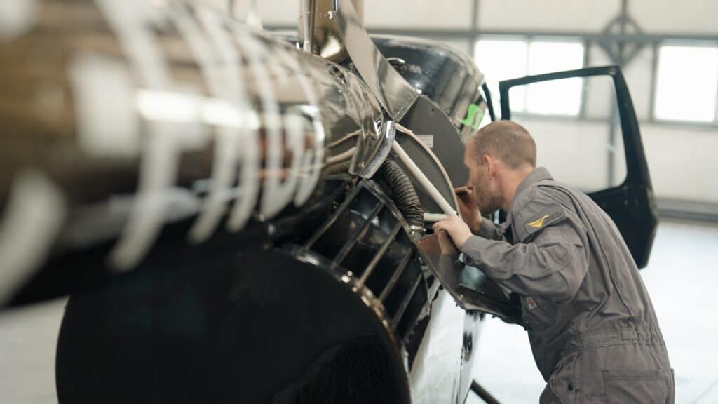 Mechanic inspecting helicopter engine inside hangar.