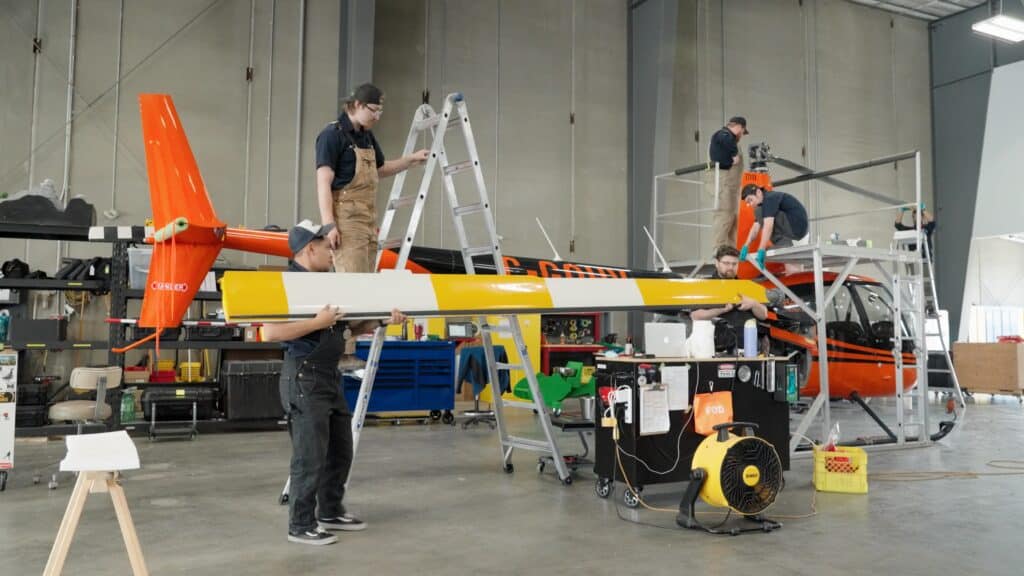 Team assembling bright orange helicopter in hangar.