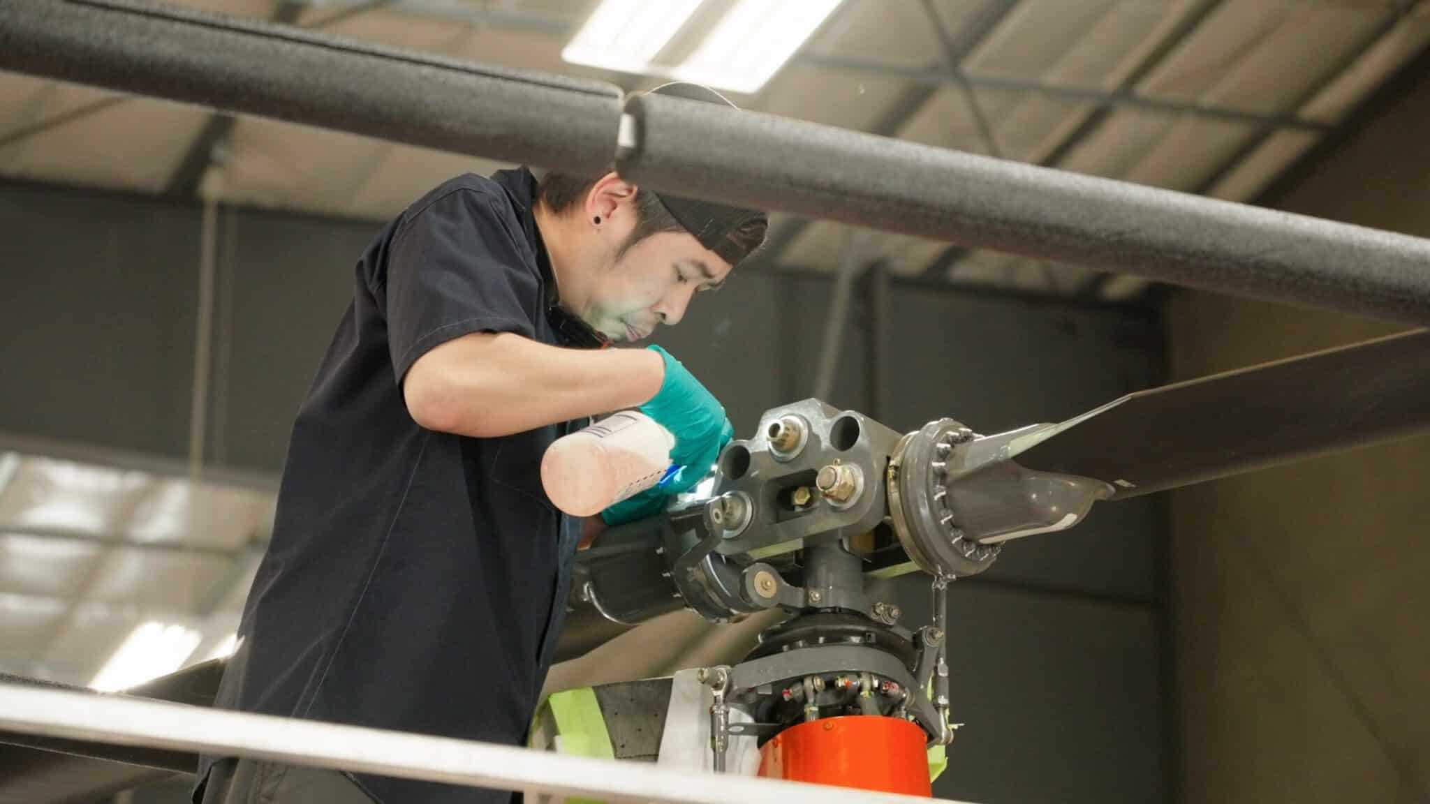 Technician inspecting helicopter rotor in hangar